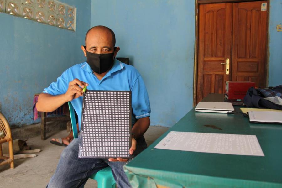 Domingos displays the small frame he uses to create documents in braille by hand.